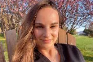 Brandi smiling in black top sitting outdoors near blooming trees on sunny day