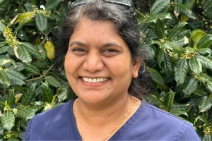 Chondra smiling in navy scrubs standing outdoors with leafy green background