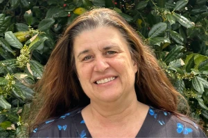 Donna smiling with long hair in butterfly print top standing by leafy bushes